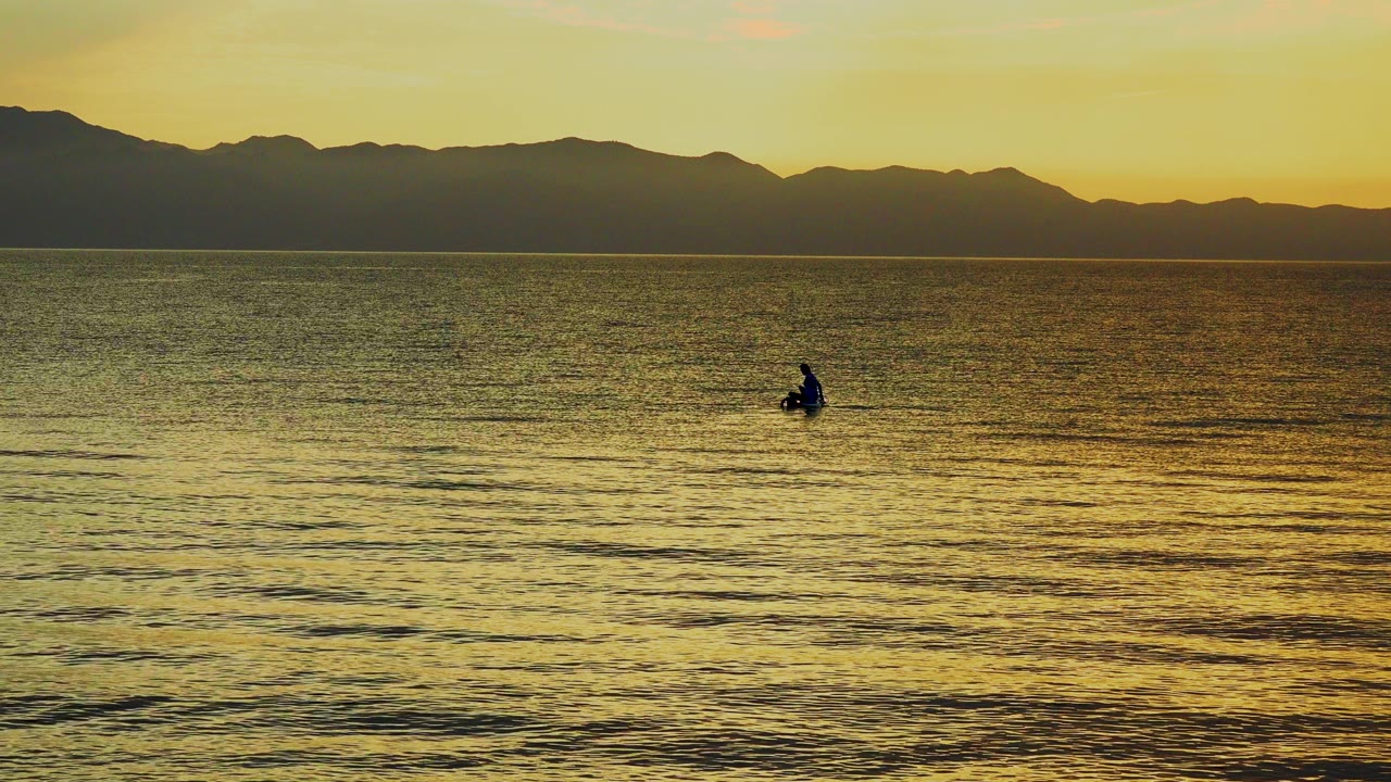 Small rower on open water below a dark mountain horizon.