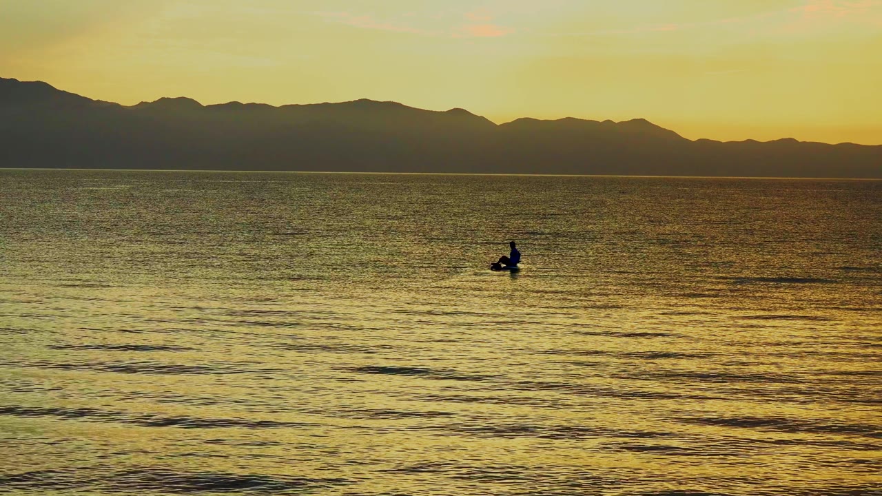 A silhouetted rower appears right of center on golden rippled water in El Sargento La Ventana, Mexico, with layered mountain shapes across the background.
