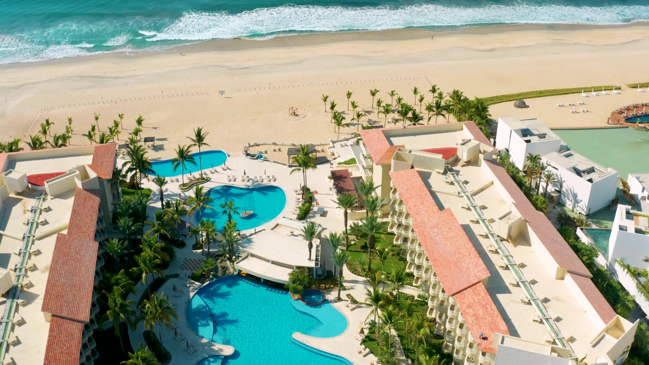 Aerial view across resort pools toward beach and waves