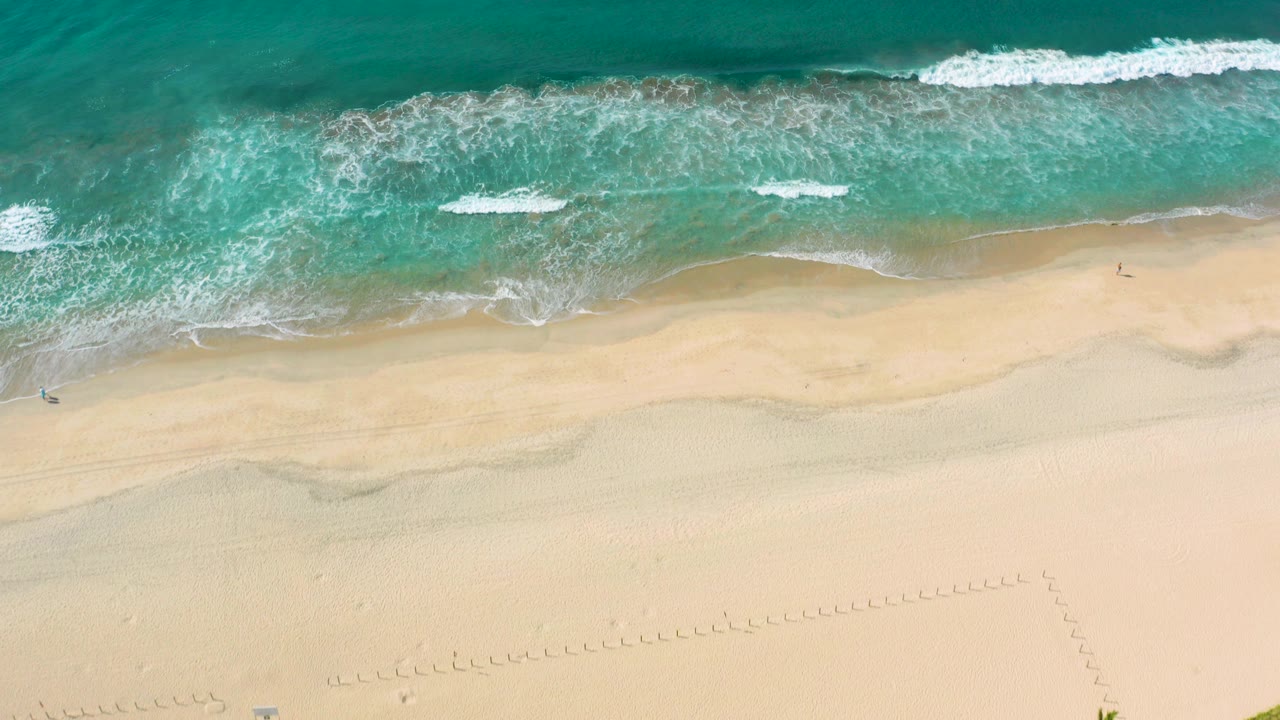 Overhead Los Cabos beach frame with turquoise water, thin white surf, pale sand below, and no visible people.