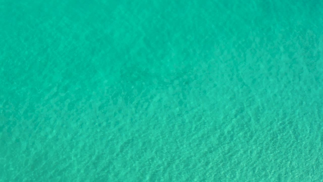 A close overhead view of teal Los Cabos water shows soft wave texture across the full frame with no visible people.