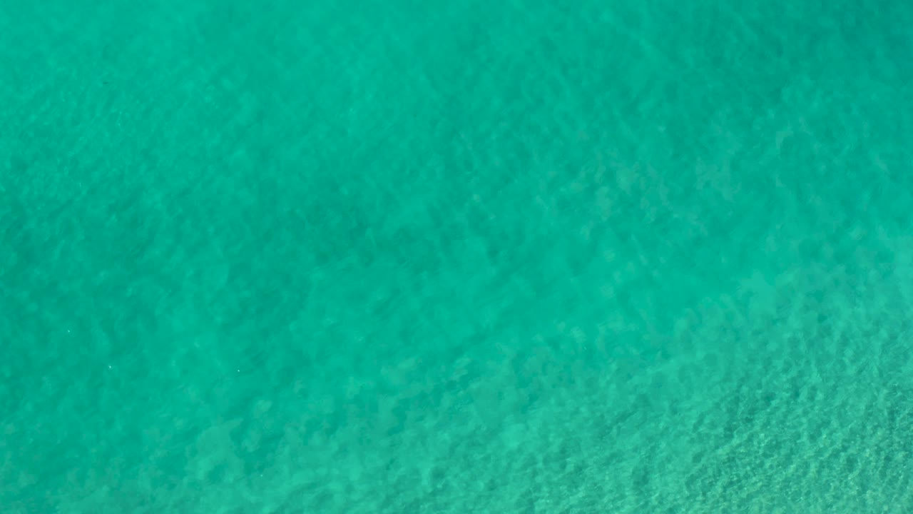 Green ocean surface in Los Cabos, Mexico shows mottled underwater texture and gentle ripples, with no visible people.