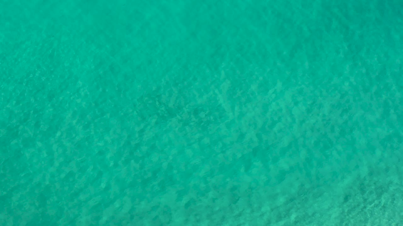 Calm turquoise water fills the Los Cabos frame with pale streaks and small surface ripples, with no visible people.
