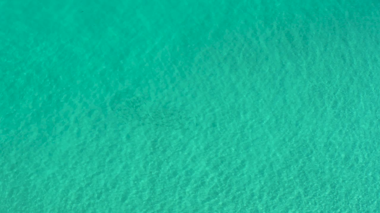 Teal green water in Los Cabos appears slightly smoother in this frame, with soft ripples spread across the full view and no visible people.
