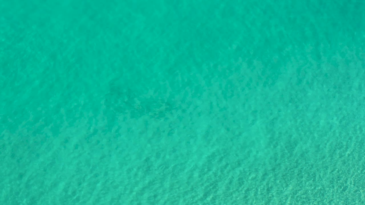 Overhead Los Cabos sea surface with green-blue color shifts, soft ripple lines, and no visible people.