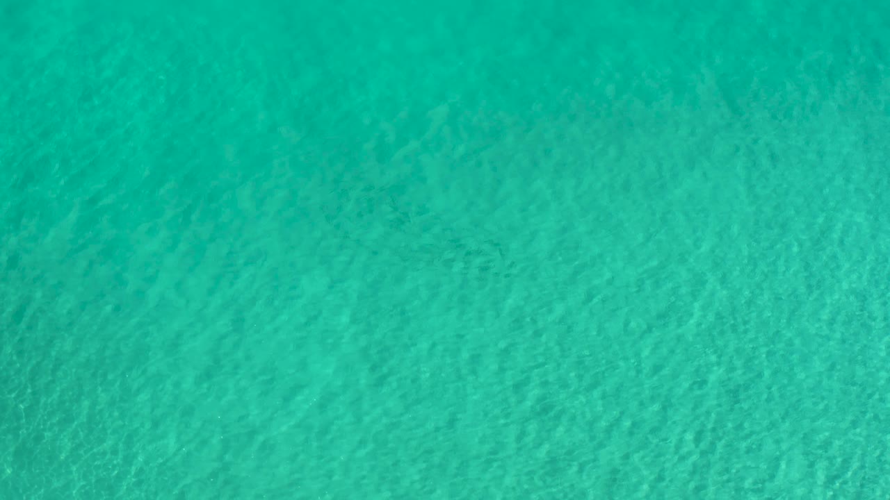 Straight-down frame of blue green pool water in Los Cabos, Mexico, where fine wave lines and darker patches create an abstract texture with no visible people.