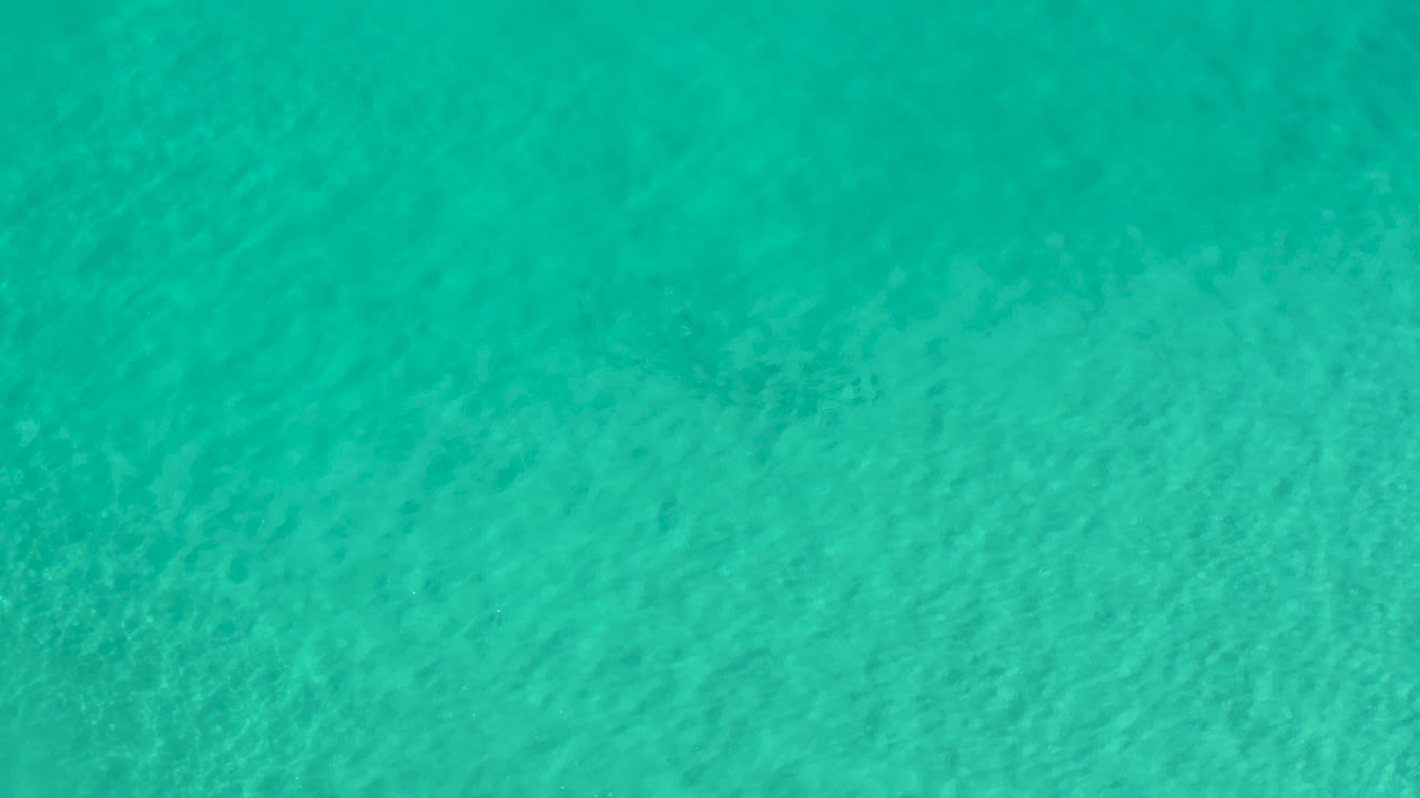 Sunlit turquoise water in Los Cabos, Mexico, shows pale wave patterns across the frame with no visible people.