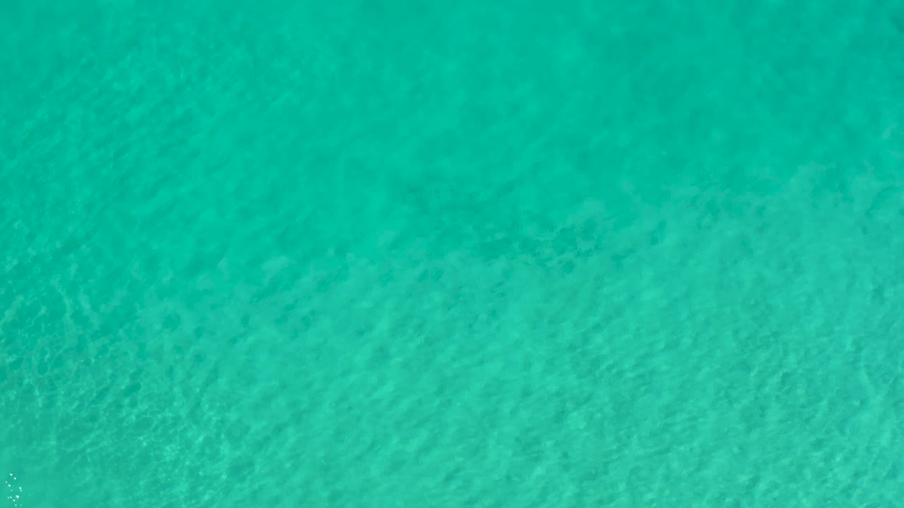 Overhead blue-green sea surface in Los Cabos, Mexico, with soft diagonal wave patterns and no visible people.