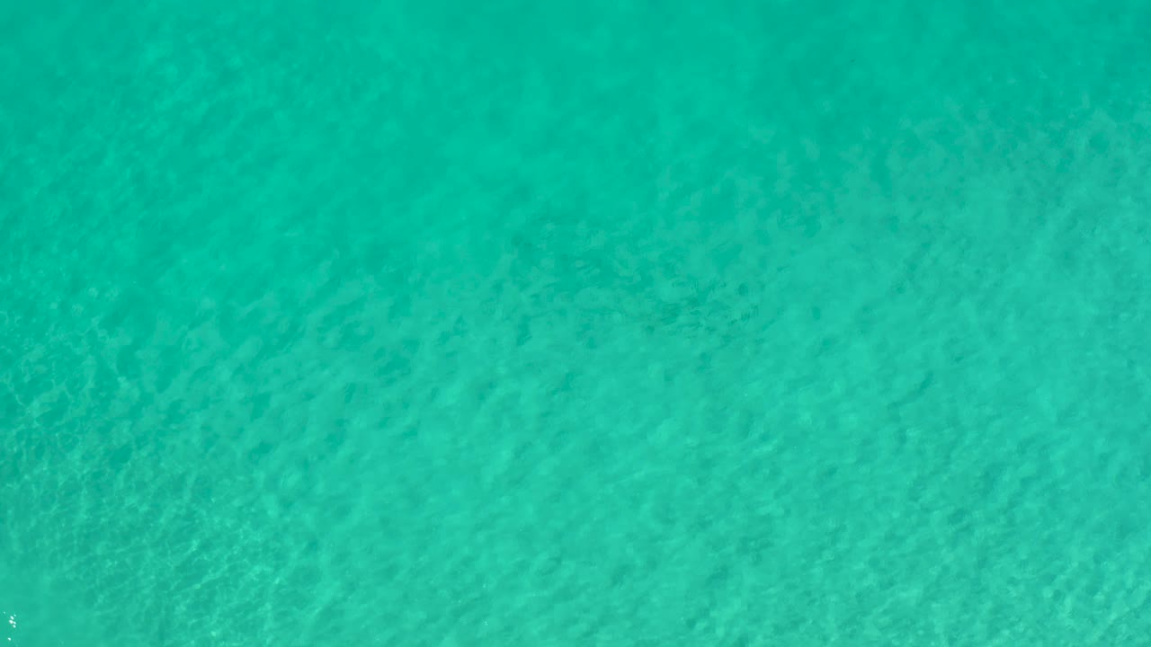 Top-down Los Cabos ocean water with small bright flecks on the surface and no visible people.
