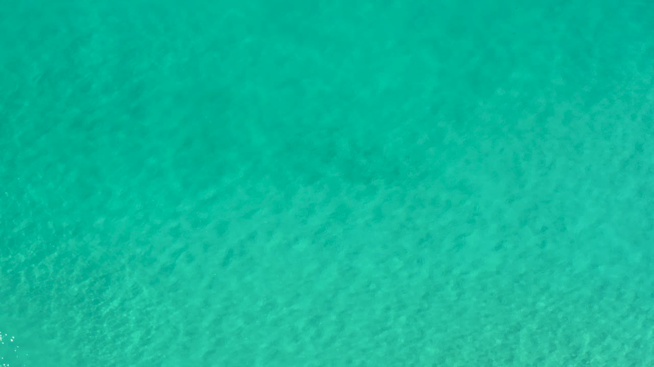 Opening frame of clear turquoise water in Los Cabos, Mexico, with fine surface ripples over a visible pale seabed and no visible people.