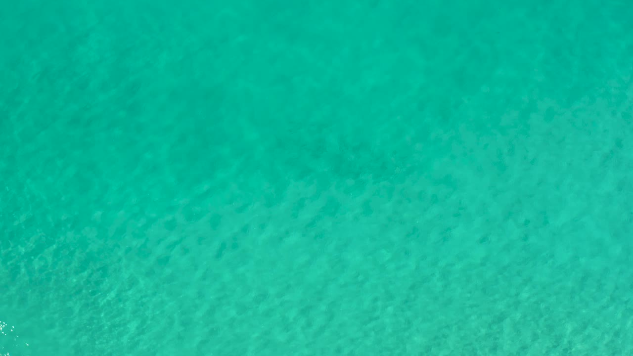 Clear blue-green water in Los Cabos, Mexico, fills the frame as faint wave texture shifts across the sandy bottom, with no visible people.