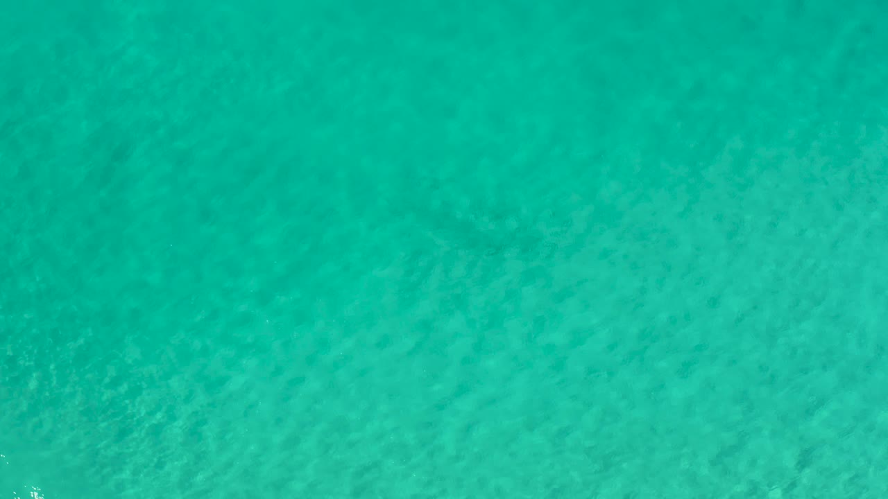 Transparent ocean water in Los Cabos, Mexico, shows gentle ripples and mottled seabed detail across the full frame, with no visible people.