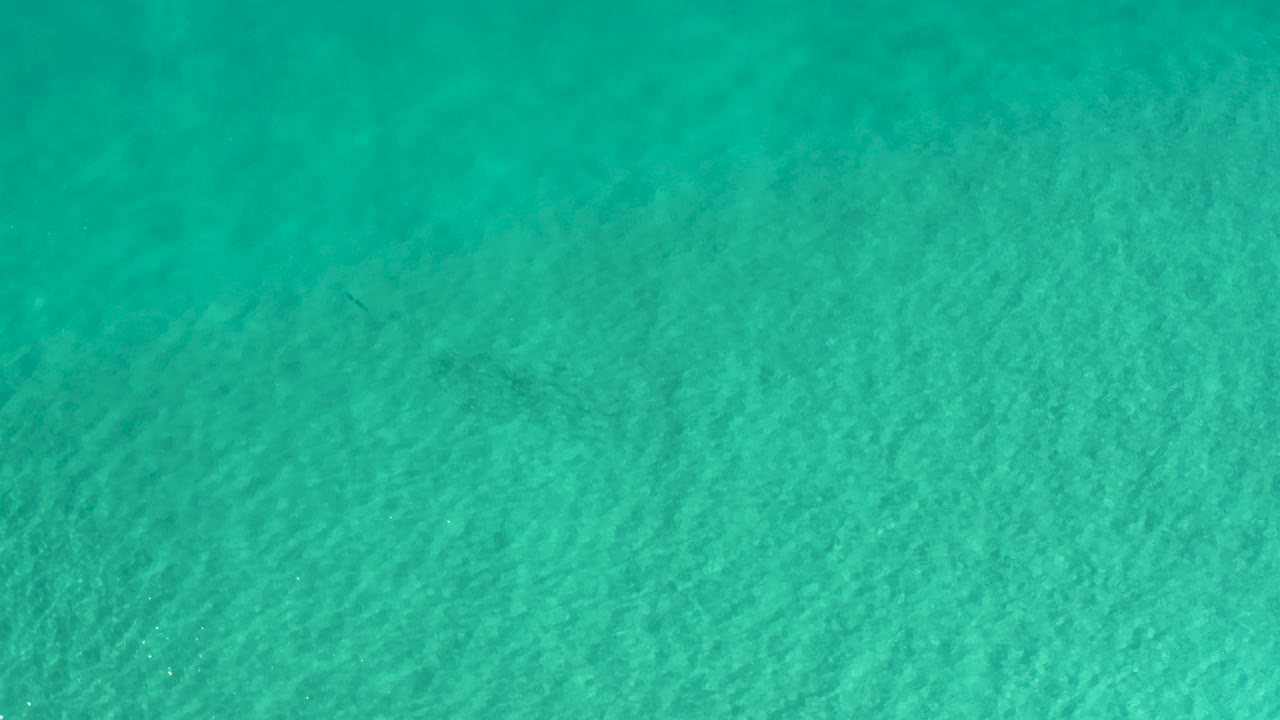 Direct overhead view of turquoise sea in Los Cabos, Mexico, with faint sandy texture below the water and no visible people.
