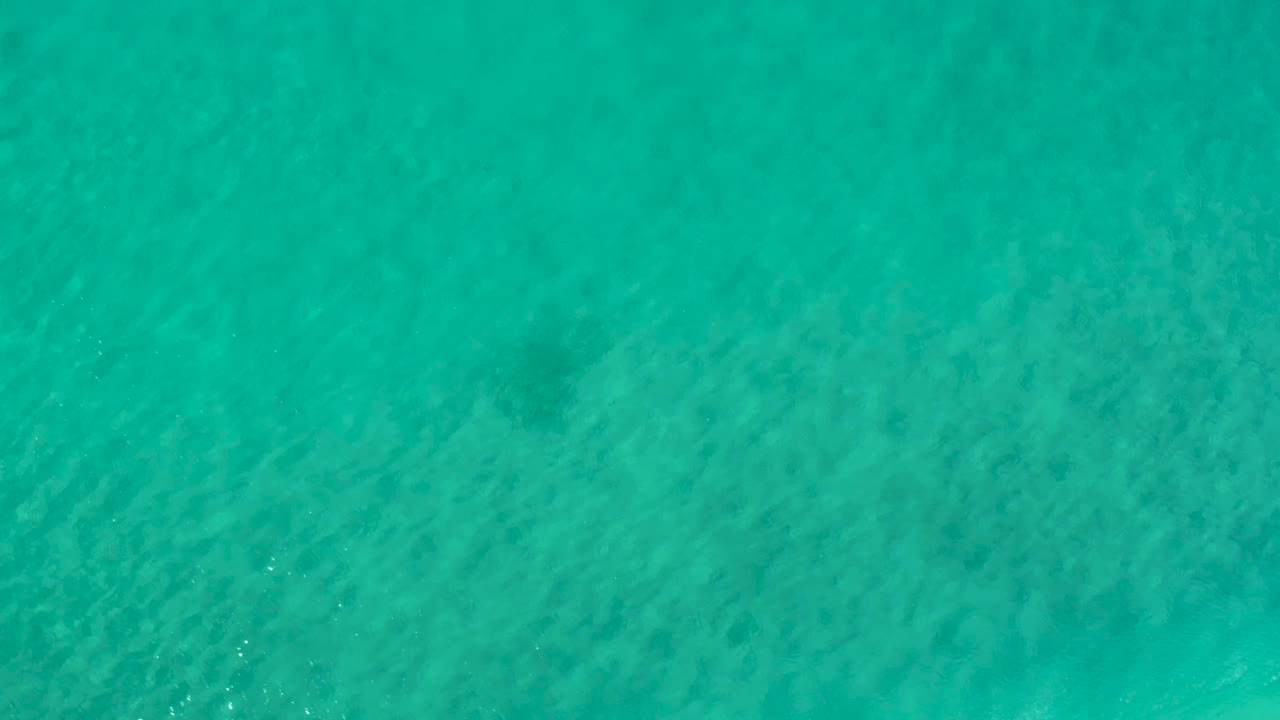 Overhead teal ocean surface in Los Cabos, Mexico, with shallow ripples and soft underwater shading, with no visible people.