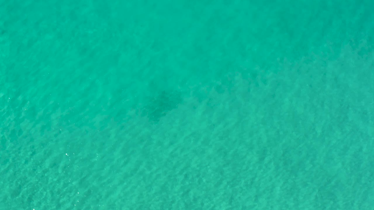 Overhead Los Cabos ocean frame with rippling teal water, pale sandy areas below, and no visible people.