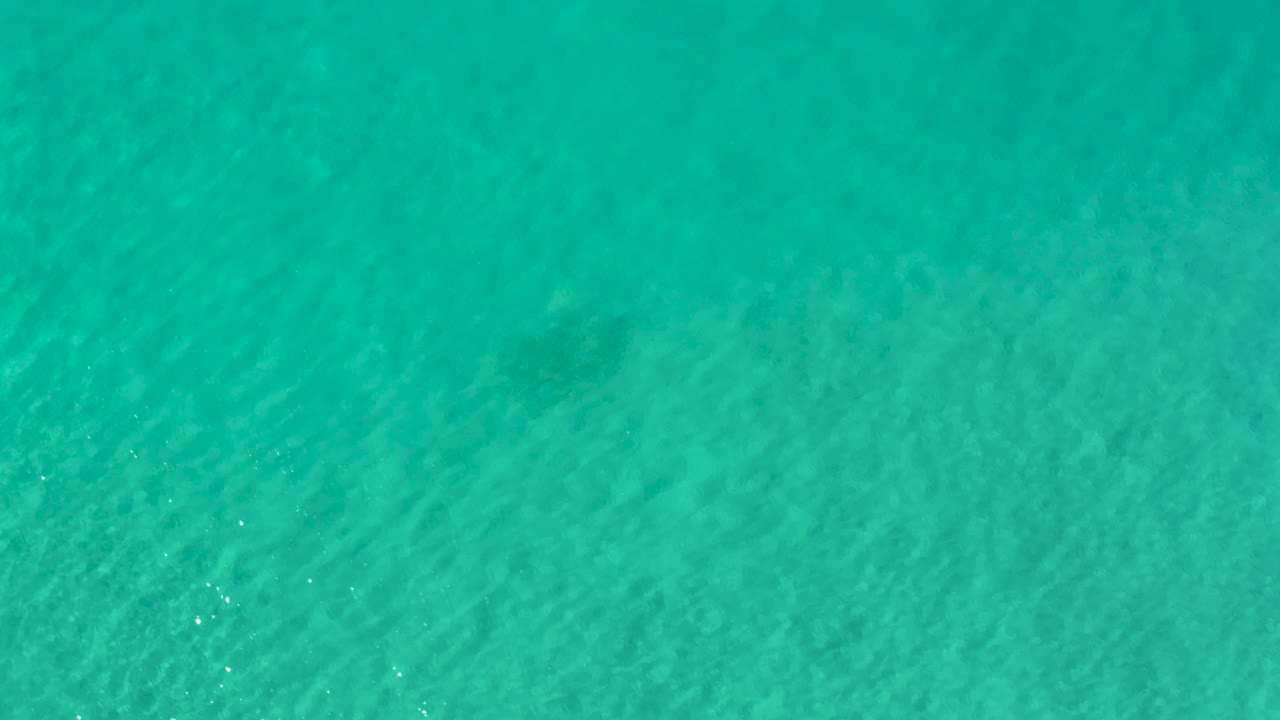 Top-down view of blue-green ocean water in Los Cabos, Mexico, with darker submerged areas and no visible people.