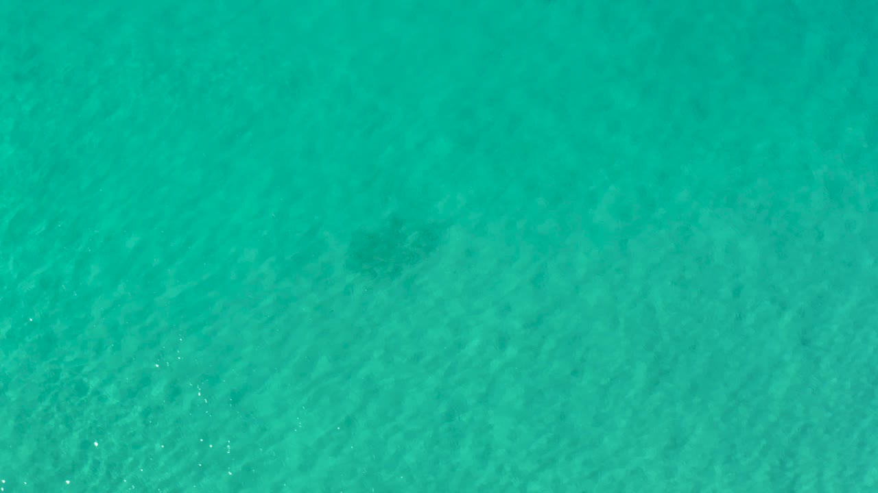 Overhead Los Cabos water surface with diagonal ripples, muted underwater shapes, and no visible people.