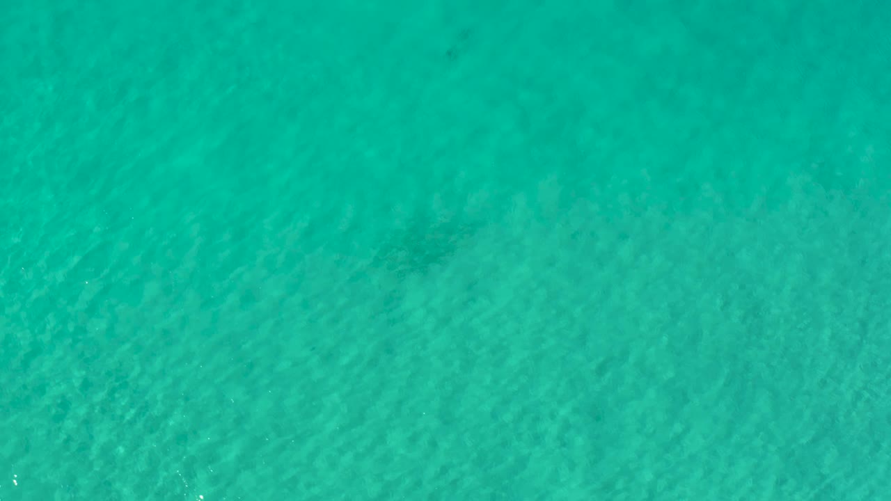 Overhead Los Cabos water frame showing turquoise-green color, subtle darker areas below the surface, and no visible people.