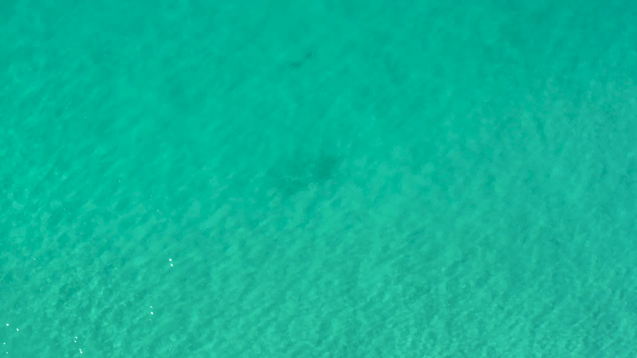 Overhead view of rippling green-blue water in Los Cabos, with small bright highlights and no visible people in the frame.