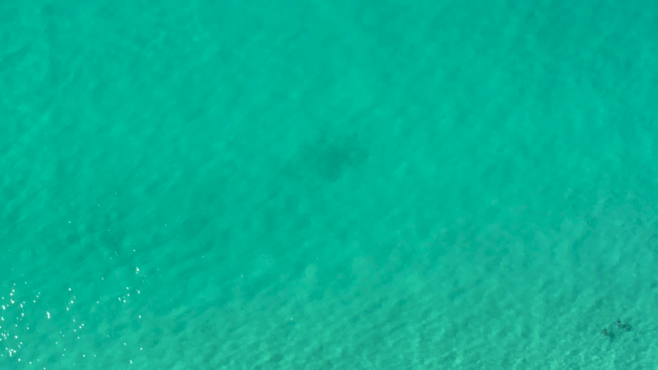 Overhead Los Cabos ocean surface with darker underwater patches, teal color, and no visible people.