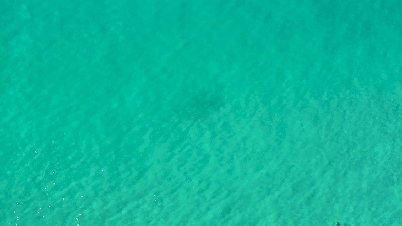 Green shallow water in Los Cabos, Mexico, with faint darker underwater marks near the center and no visible people.