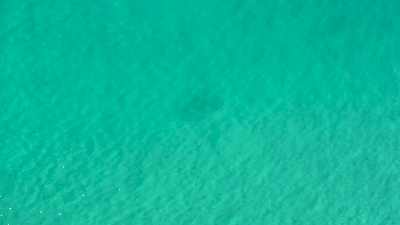 Top-down view of turquoise green sea water in Los Cabos, Mexico, with soft ripple bands and no visible people.