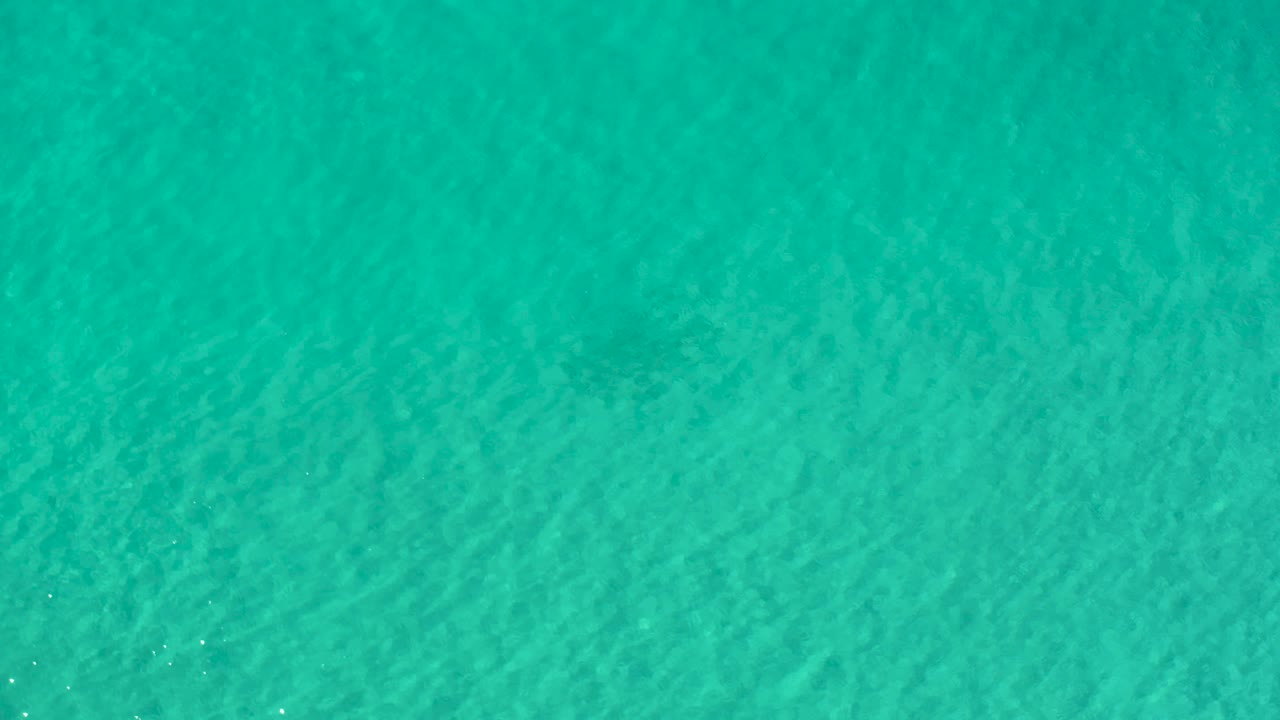 Clear turquoise water in Los Cabos, Mexico, shows soft ripples and a few tiny sun glints scattered across the surface, with no visible people.