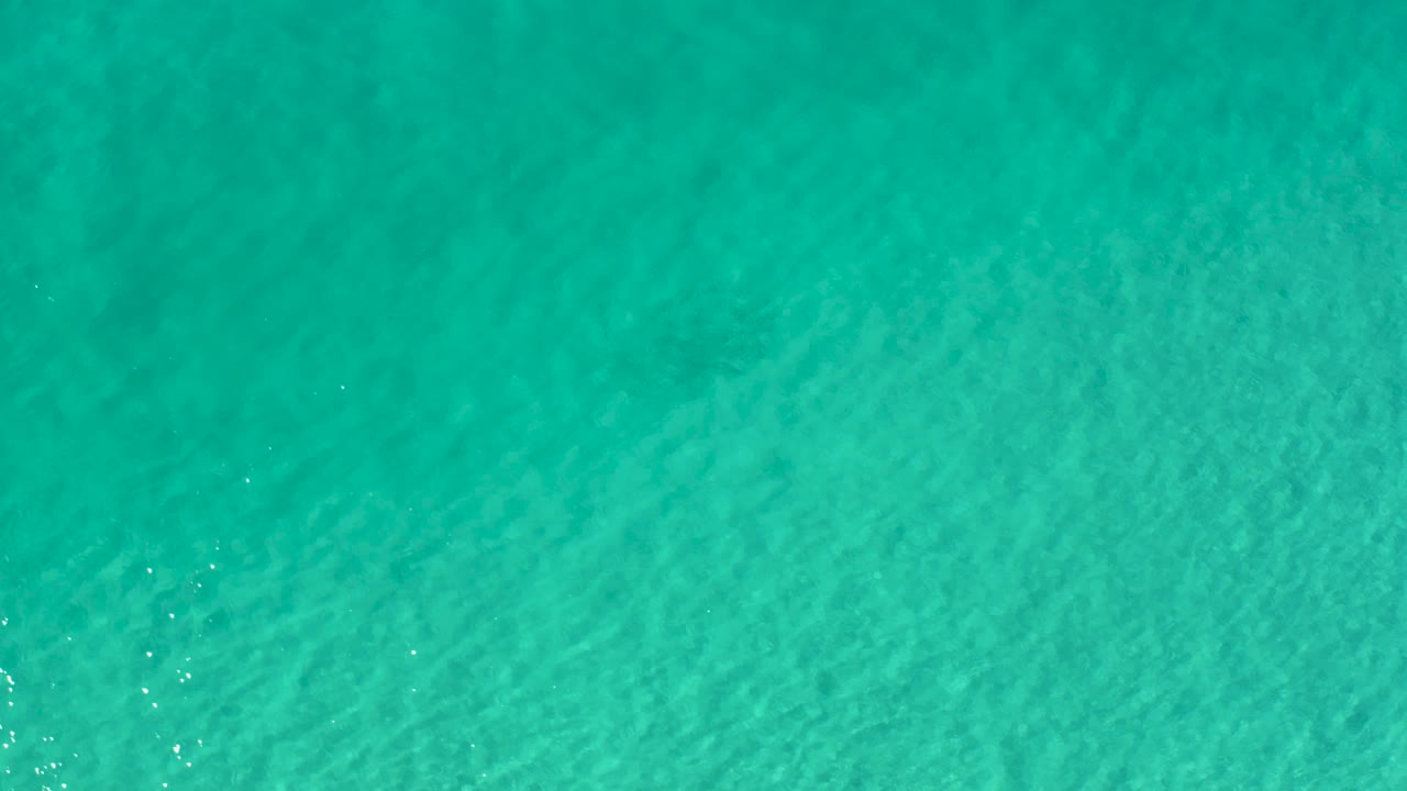 An overhead Los Cabos water view shows a slightly darker teal surface with soft ripple movement and no visible people.