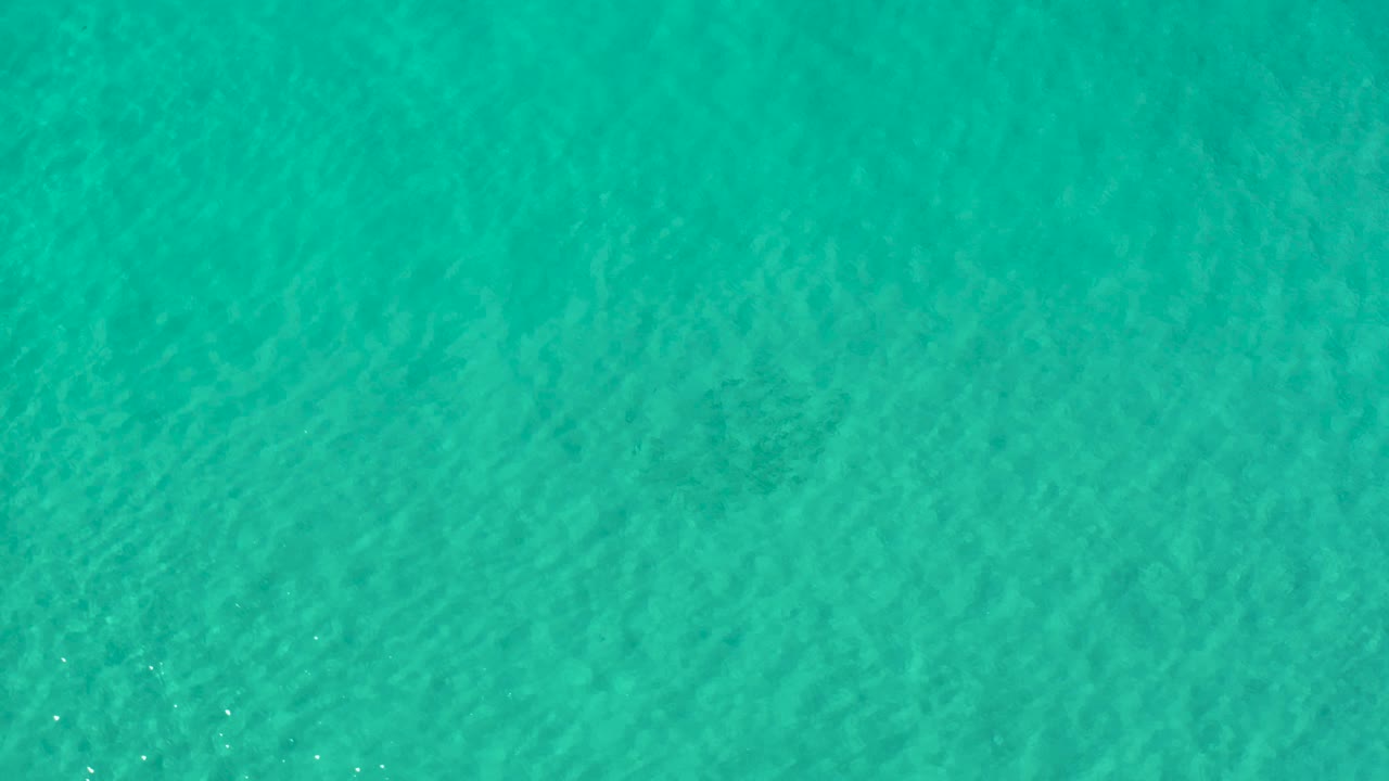 Blue-green ocean water in Los Cabos, Mexico, appears slightly darker across the upper area, with small light sparkles on the surface and no visible people.