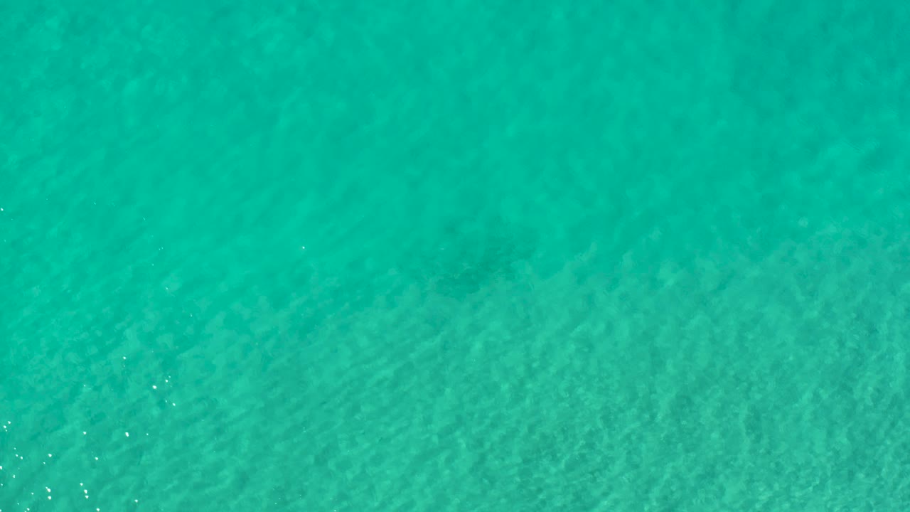 Top-down Los Cabos sea view showing shallow turquoise color, faint seabed variation, and no visible people.