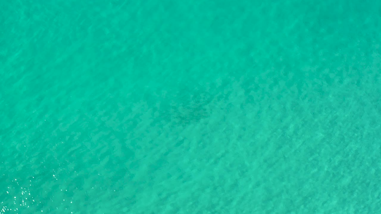 Blue-green Los Cabos ocean water viewed from above, with small bright highlights near the left edge and no visible people.