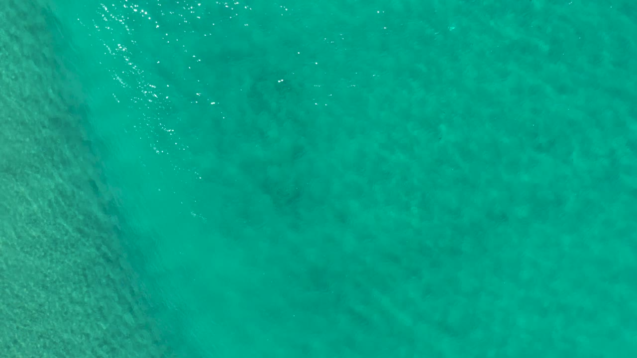 Blue-green coastal water fills the frame in Los Cabos, Mexico, with a brighter band of reflected light near the top and no visible people.