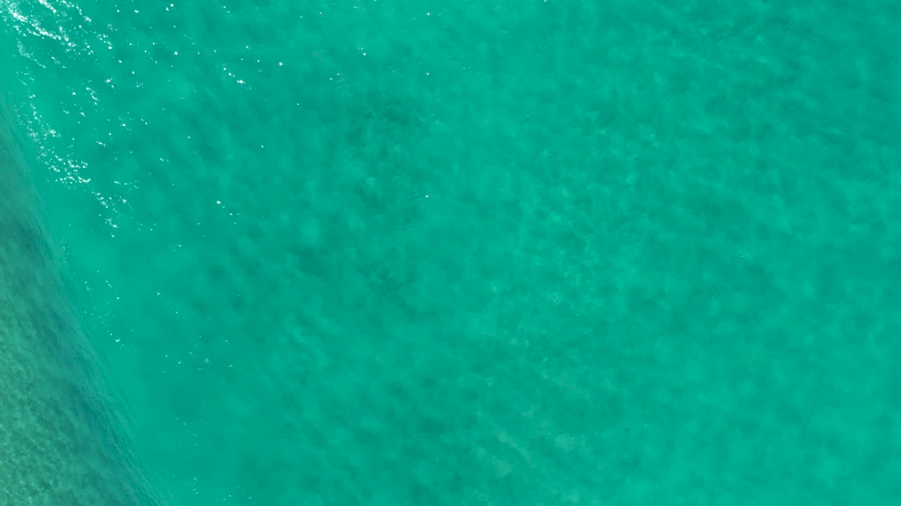 Rippling teal water with soft darker shapes below the surface.