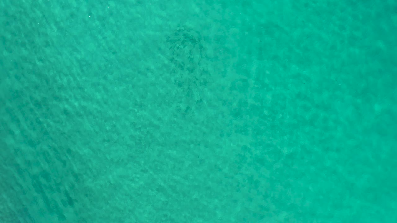 Turquoise ocean water in Los Cabos, Mexico, shows darker underwater patches below the rippled surface and no visible people.