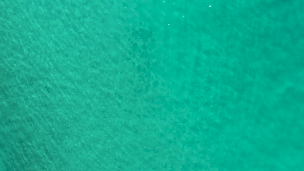 Blue-green water in Los Cabos, Mexico, fills the overhead frame with diagonal ripple lines and no visible people.