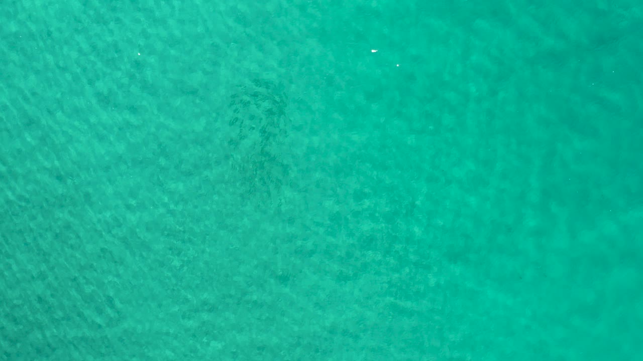 Overhead view of turquoise ocean water in Los Cabos, Mexico, with fine surface ripples, faint darker underwater patches, and no visible people.