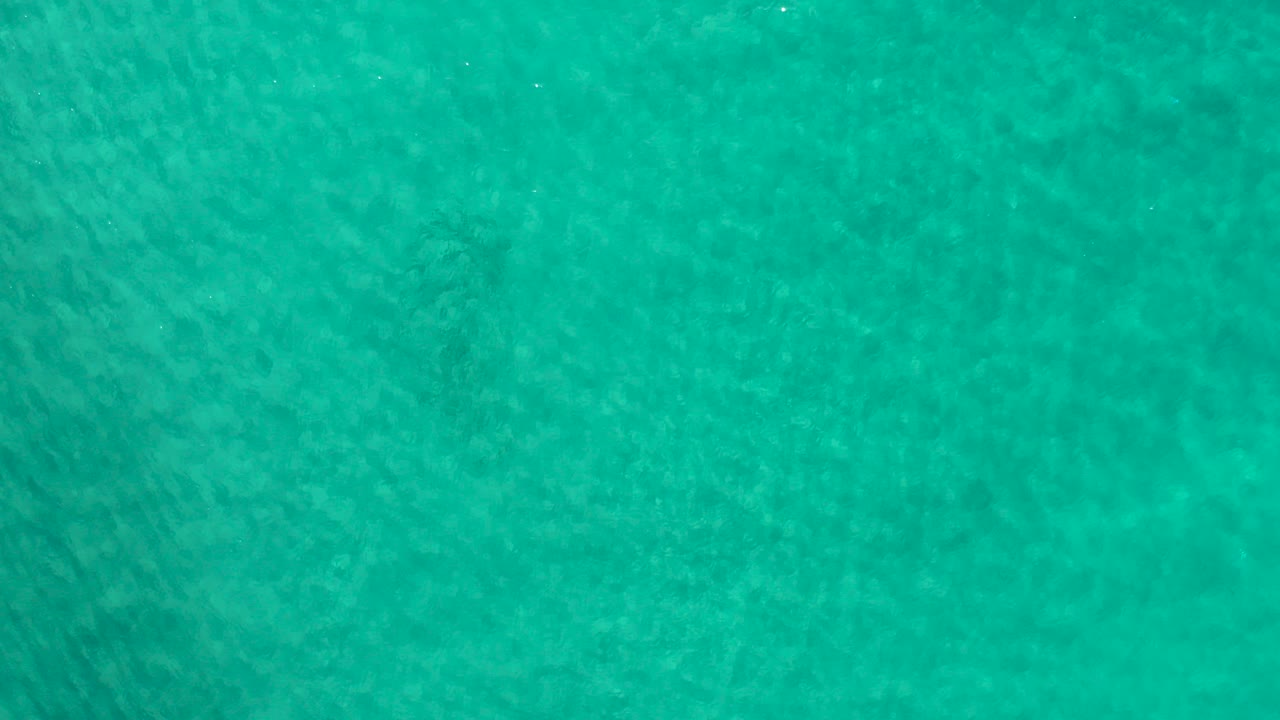 Overhead view of aquamarine ocean water in Los Cabos with soft ripples, faint darker underwater texture, and no visible people.