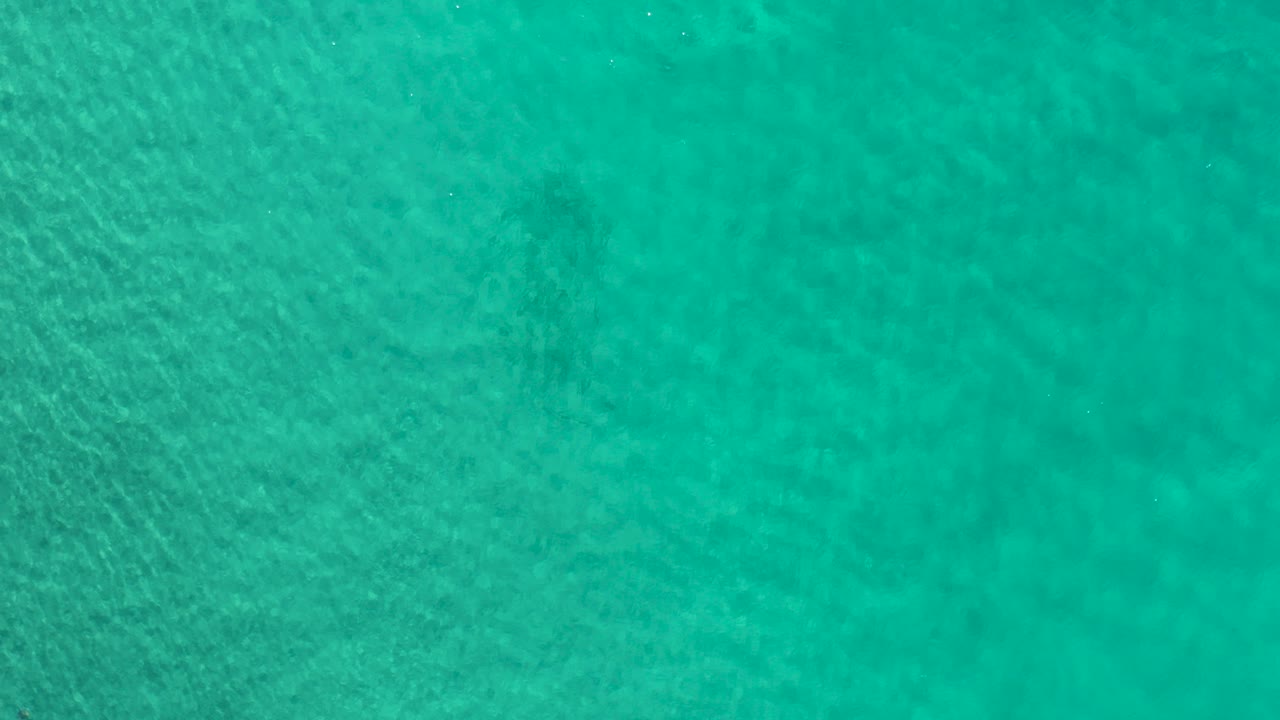 Clear turquoise-green water in Los Cabos, Mexico fills the opening frame with fine ripples, faint darker shapes below the surface, and no visible people.