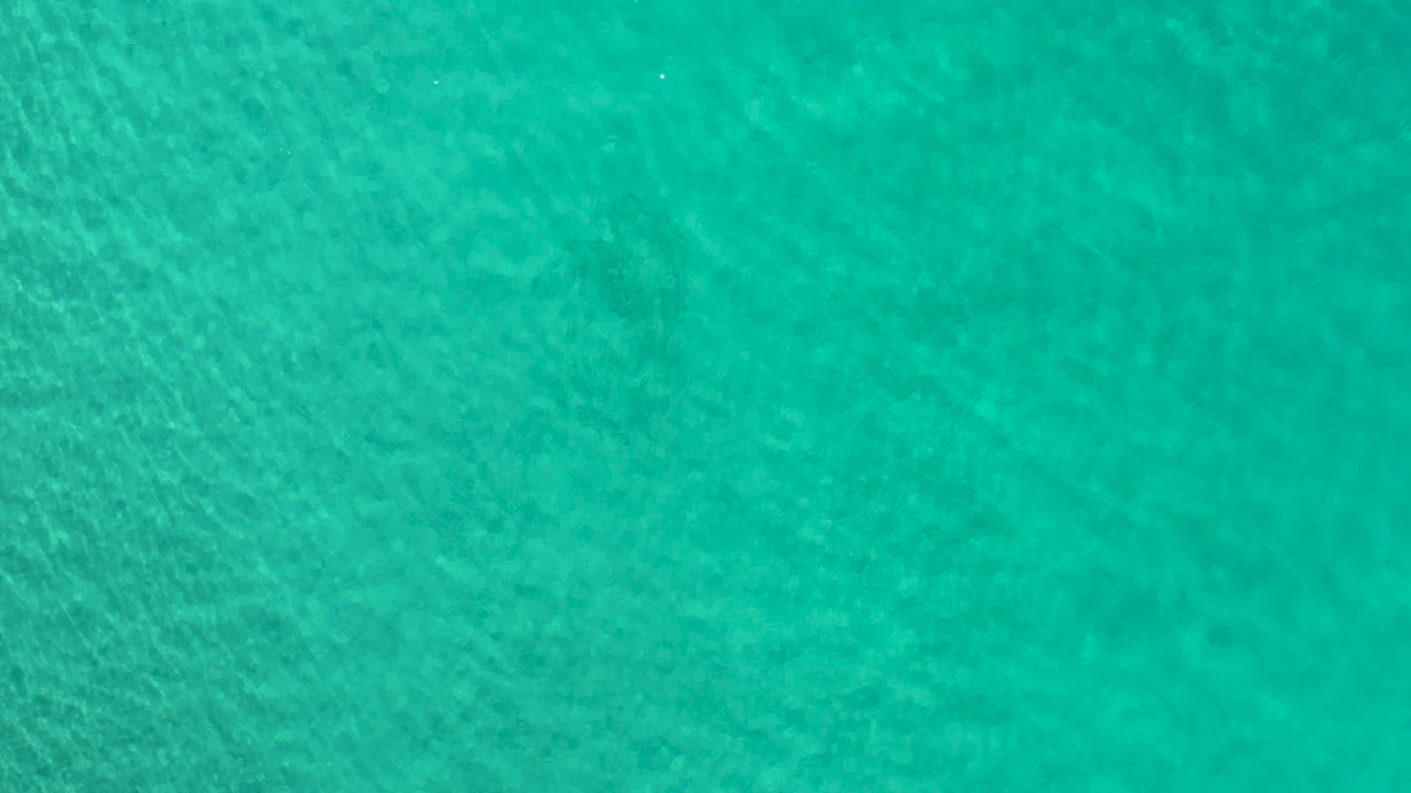 Overhead view of clear turquoise seawater in Los Cabos, Mexico, with faint darker underwater patches and no visible people.