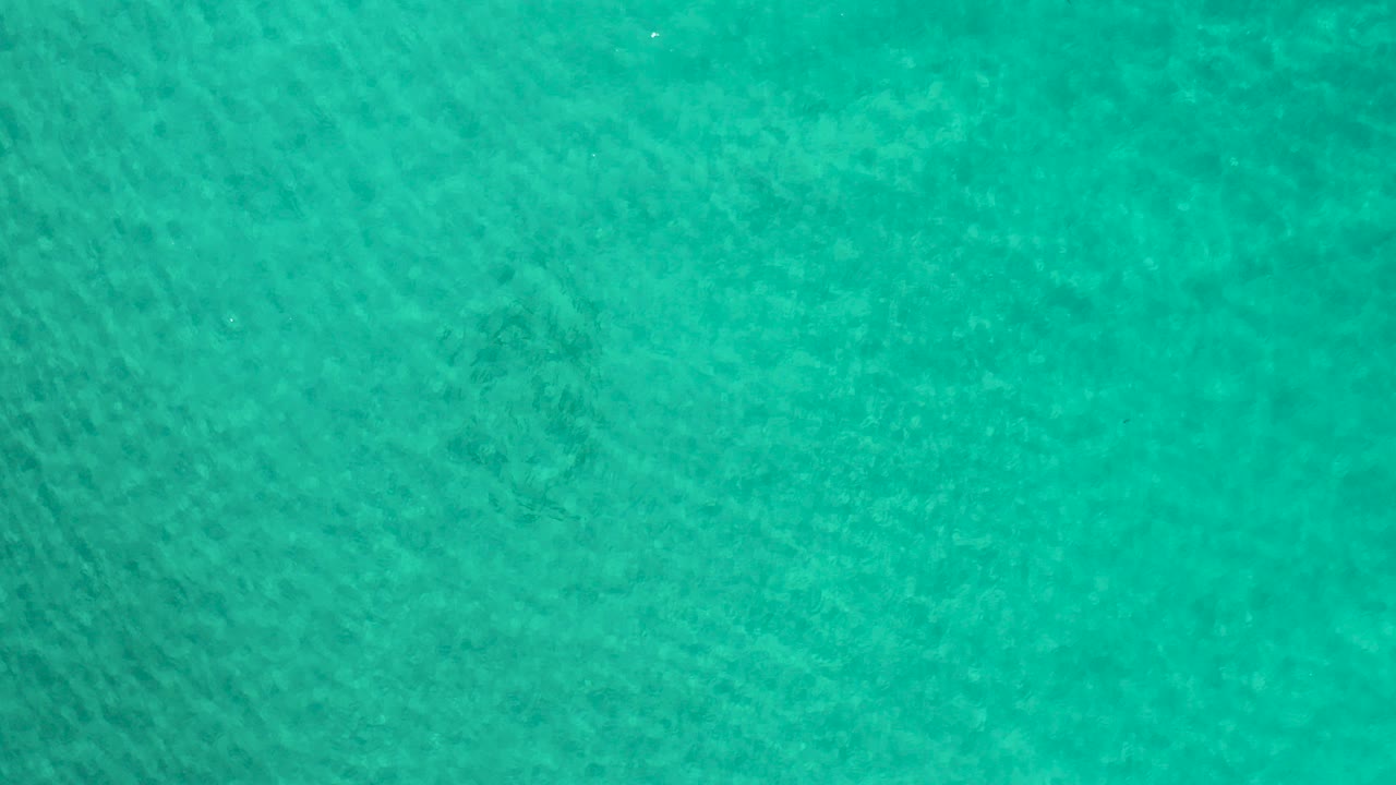 Top-down view of teal-green ocean water in Los Cabos, Mexico, with faint surface ripples and no visible people.