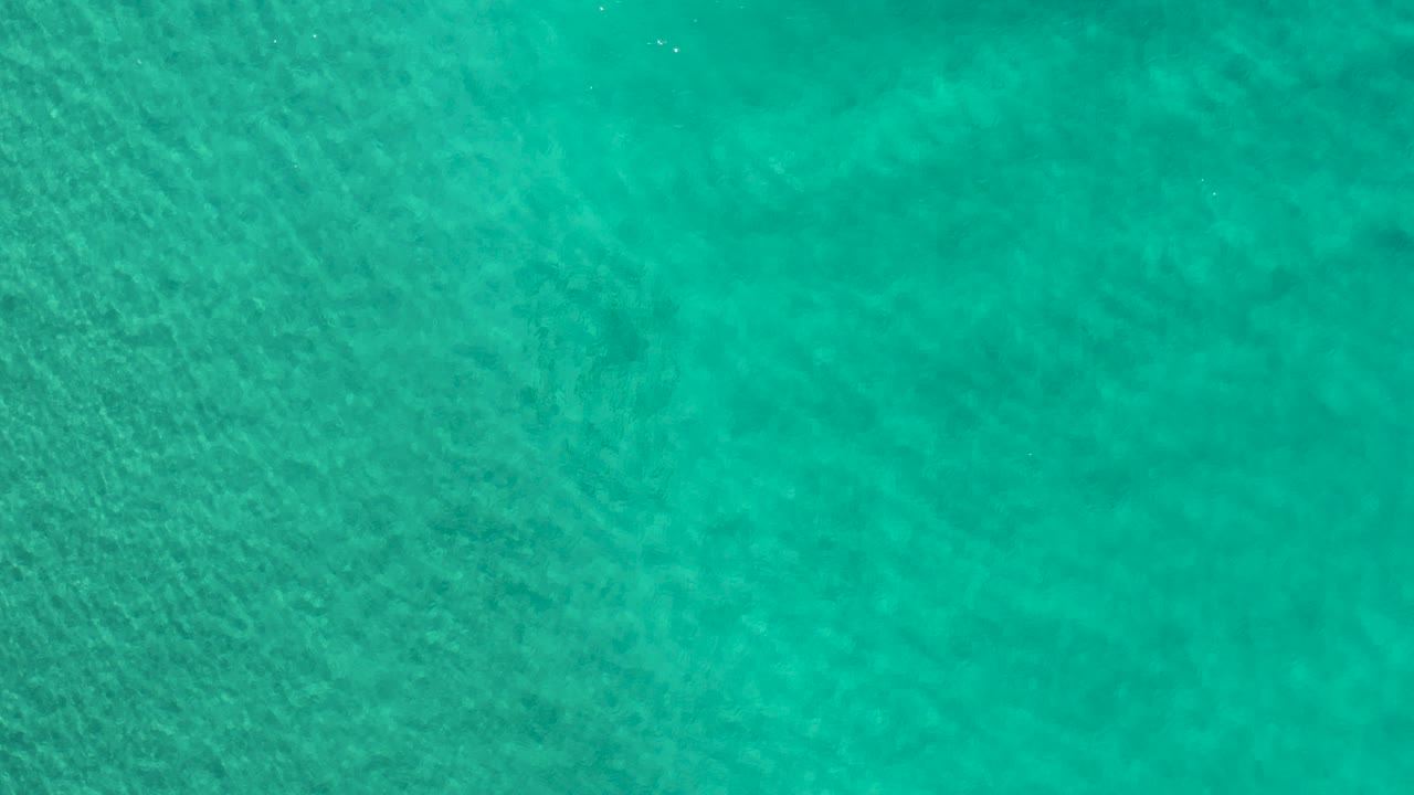 Overhead view of green ocean water in Los Cabos, Mexico, with faint darker patches below the surface and no visible people.