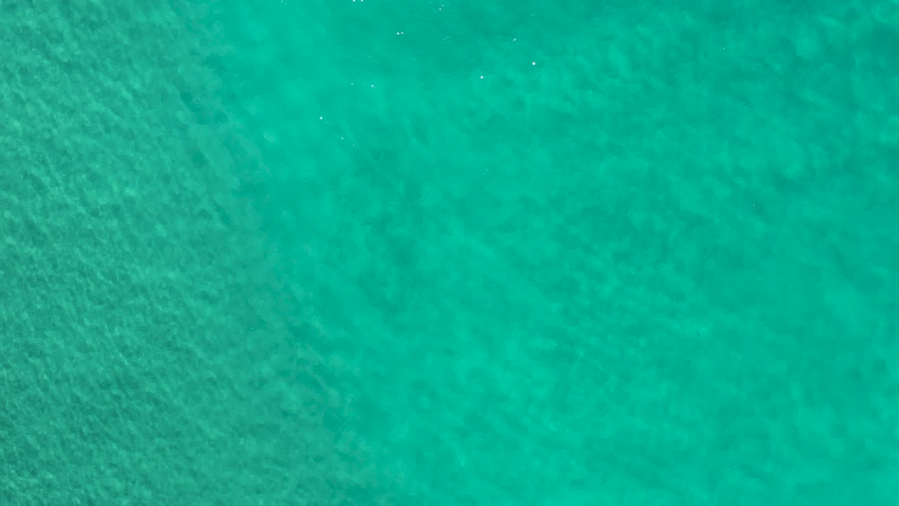 Aerial green sea water over Los Cabos, Mexico, showing mottled underwater texture beneath a lightly rippled surface and no visible people.
