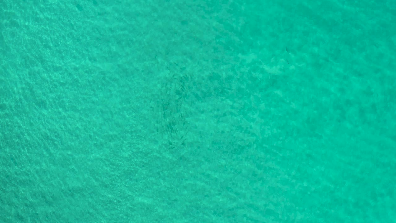 Turquoise Los Cabos ocean surface fills the frame, with faint darker areas under the water and no visible people.