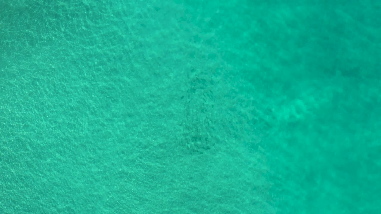Shallow blue-green water fills the frame in Los Cabos, Mexico, with soft ripples crossing faint darker seabed areas and no visible people.