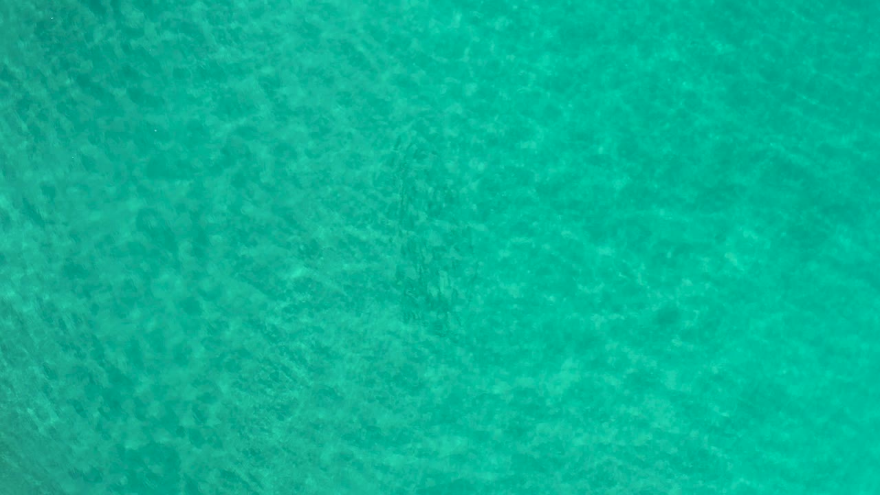Turquoise ocean surface seen from above in Los Cabos, Mexico, with faint wave texture crossing the frame and no visible people or objects.