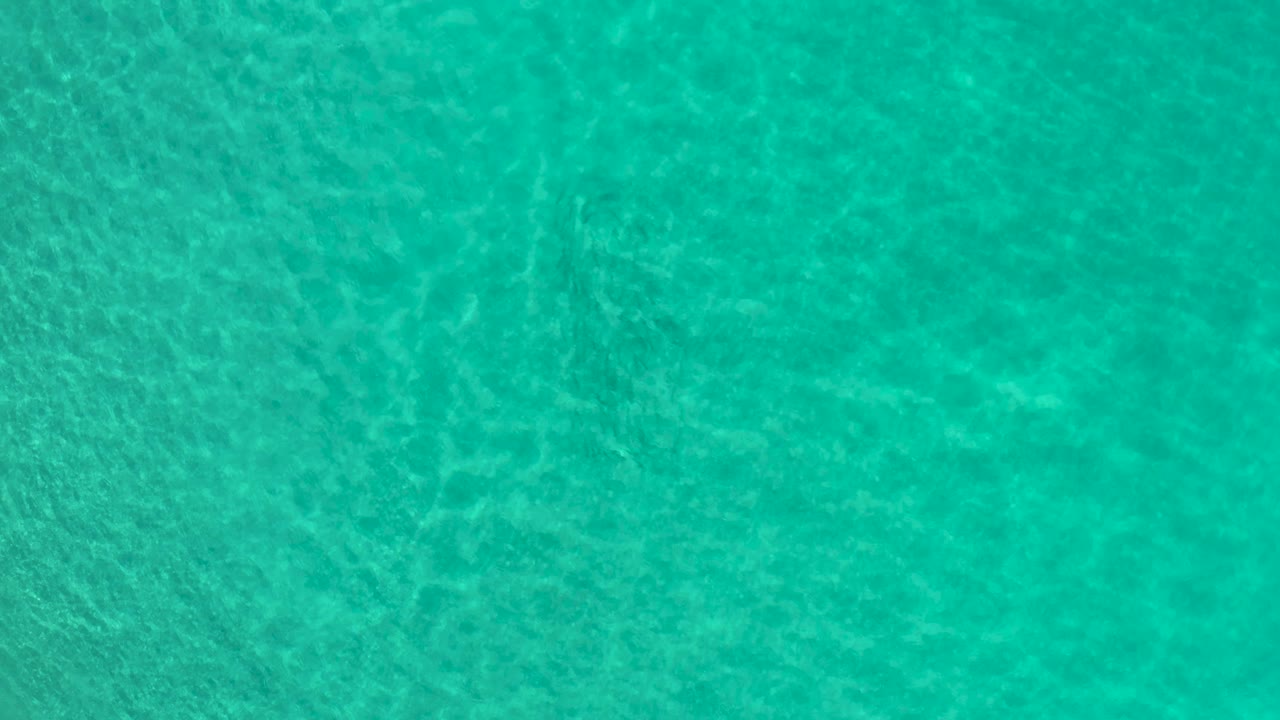 Clear teal ocean water fills the frame in Los Cabos, Mexico, with brighter ripple lines crossing the visible bottom and no visible people.