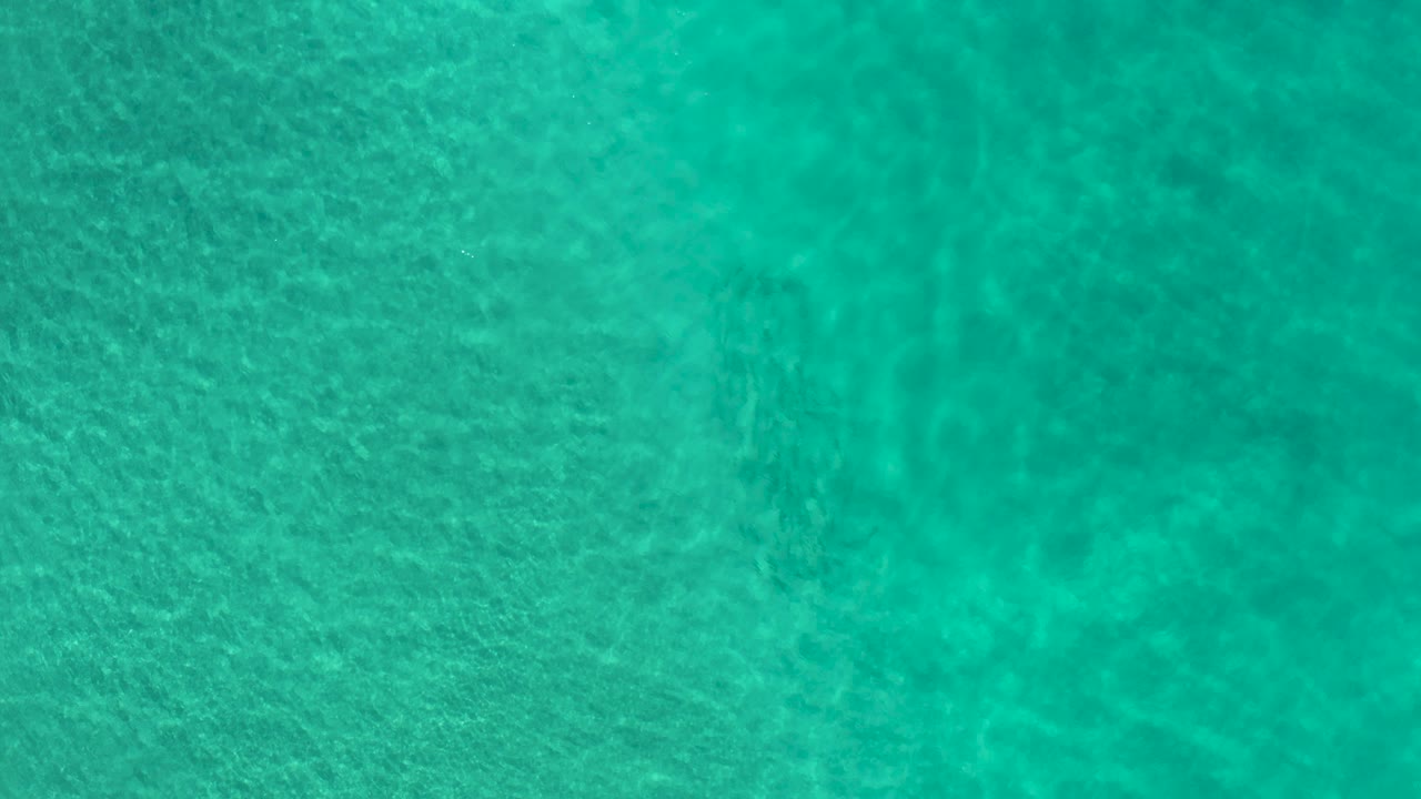 Overhead turquoise ripples pass across sandy shallows in Los Cabos, Mexico, with a slightly darker water patch and no visible people.