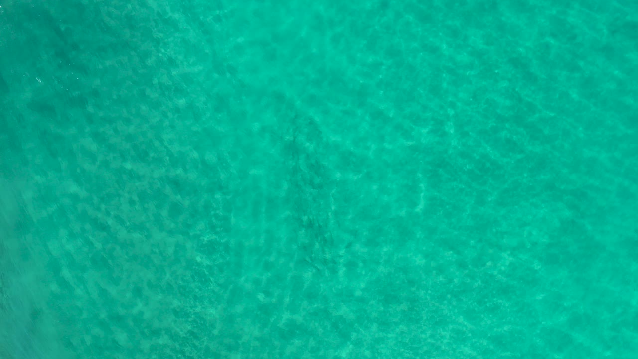 Overhead view of turquoise green sea water in Los Cabos, Mexico, with faint sandy texture below the ripples and no visible people.