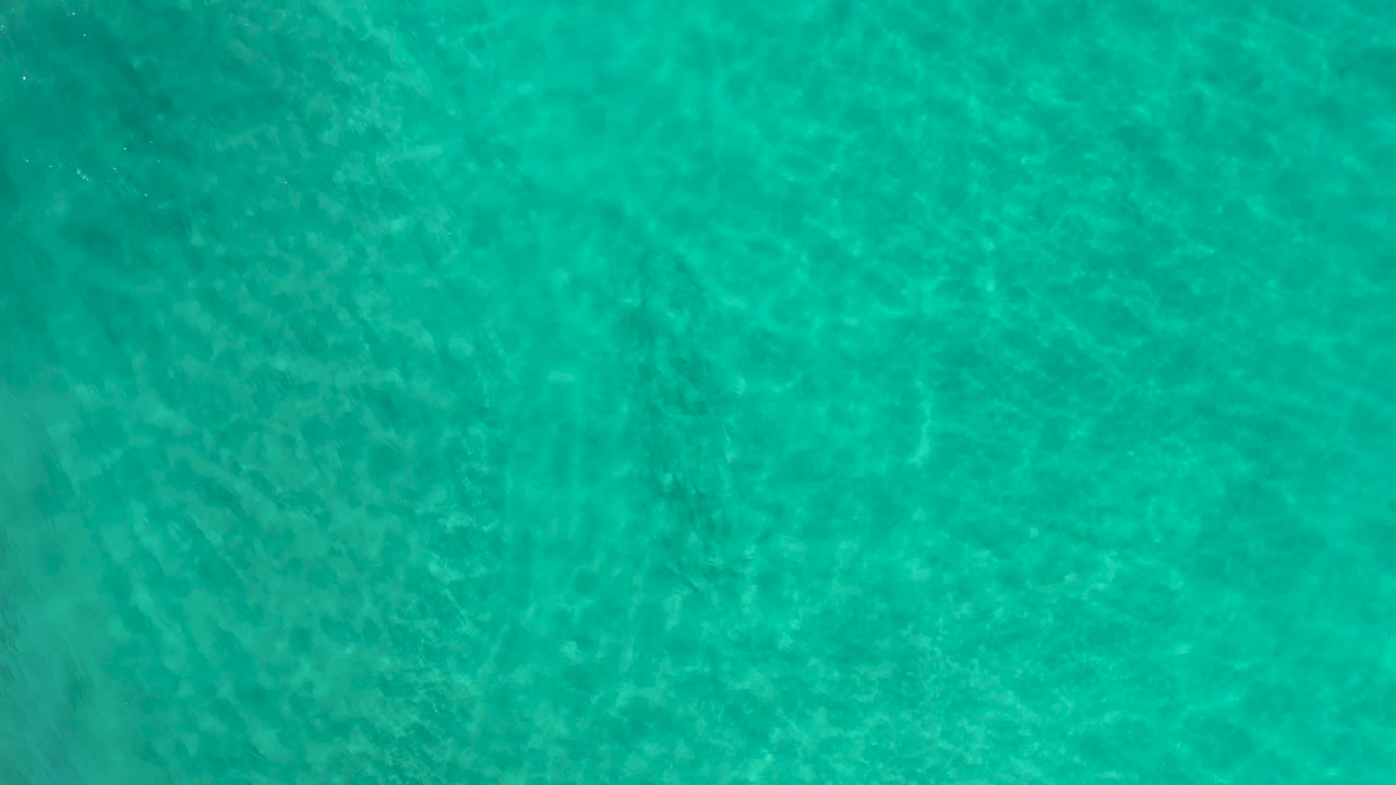 Clear green ocean surface in Los Cabos, Mexico, showing soft ripple patterns across shallow water and no visible people.