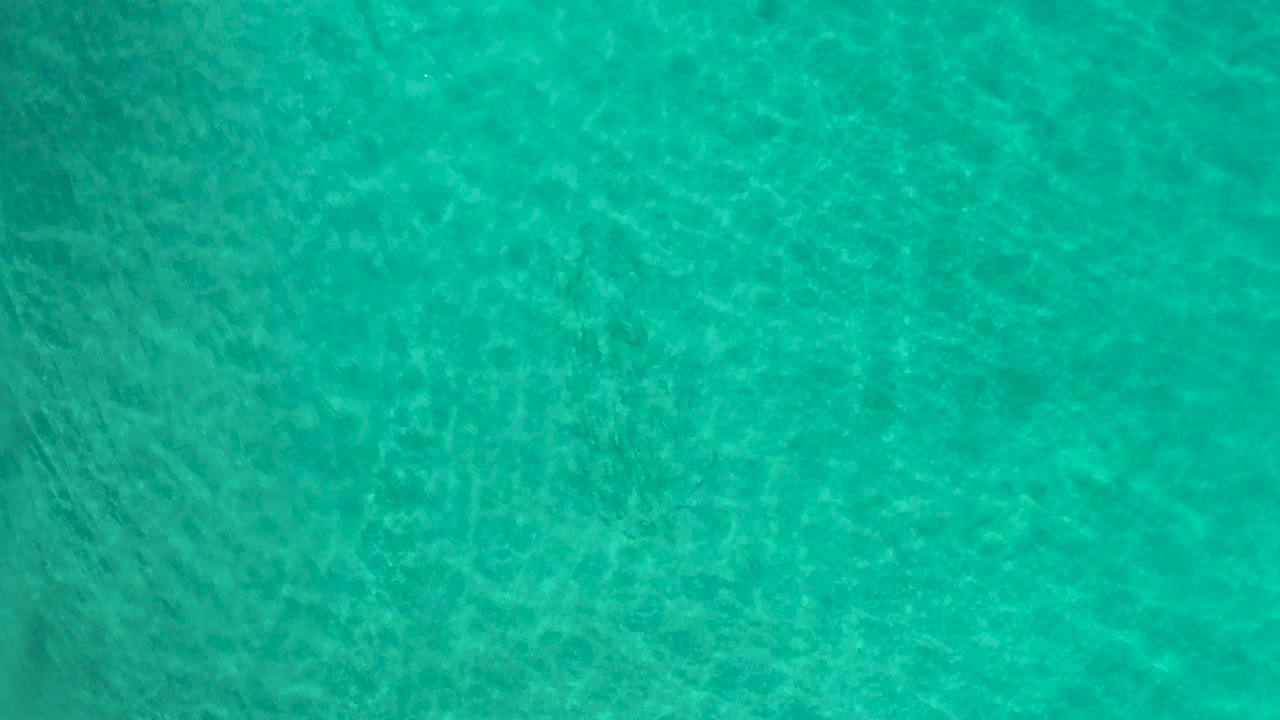 Green sea water in Los Cabos, Mexico, with brighter ripple highlights over a pale underwater bed and no visible people.